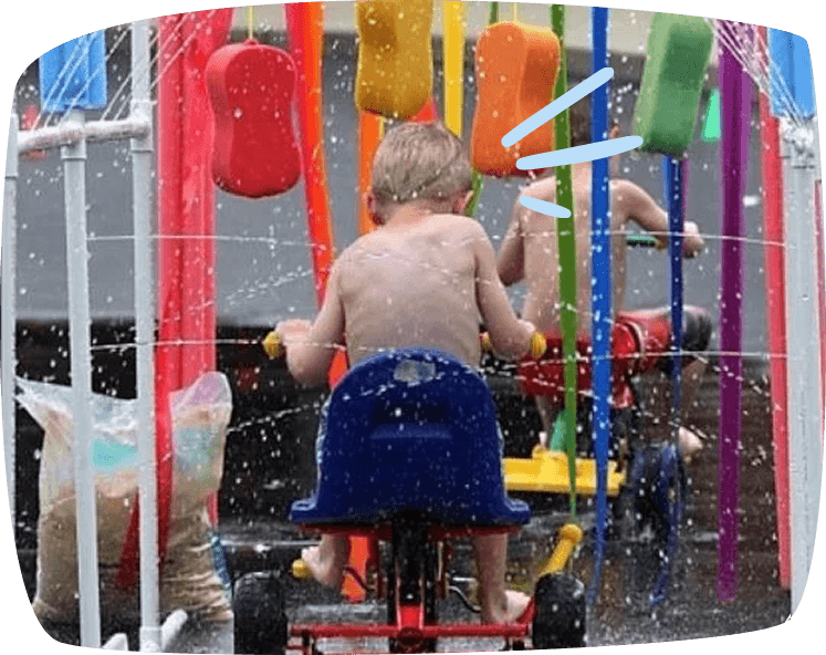 Enfant traversant une station de lavage faite maison pour tricycles, avec des éponges et de l’eau