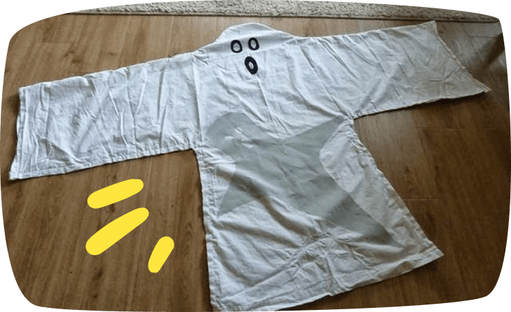 Un drap blanc posé à plat sur un parquet, décoré d'yeux et d'une bouche dessinés en noir pour créer un déguisement de fantôme fait maison.